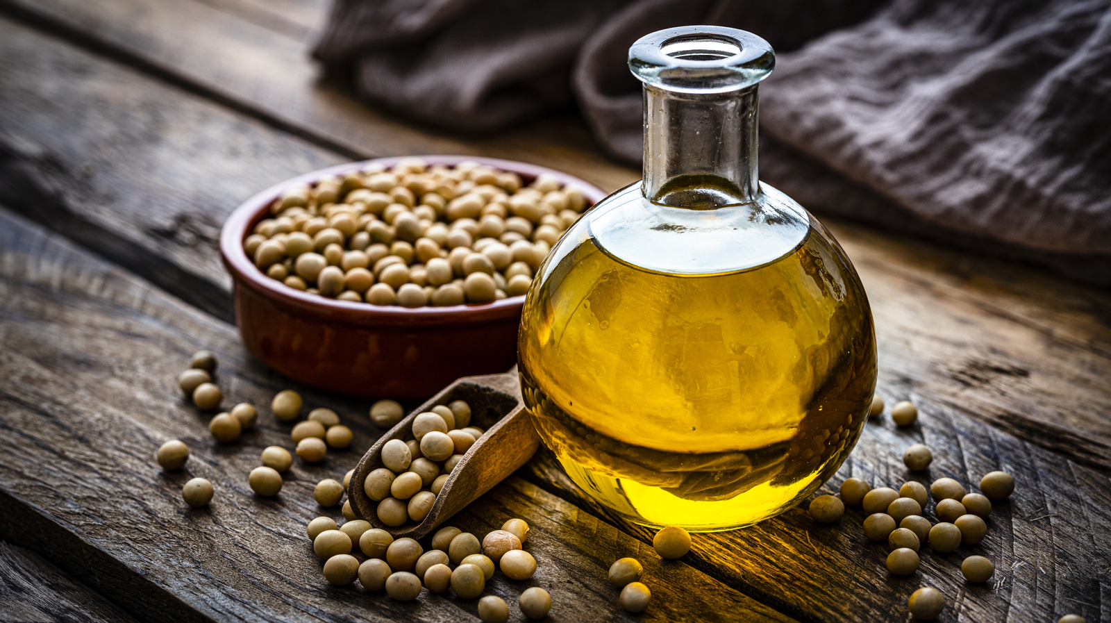 Close up view of a glass bottle filled with soy oil shot on rustic wooden table. A bowl with dried soybeand complete the composition Plant-based nutrition concept. High resolution 42Mp studio digital capture taken with Sony A7rII and Sony FE 90mm f2.8 macro G OSS lens